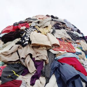 textile pollution, fast fashion industry waste, old clothing cloth fabric garment trash garbage pile stack heap  background, concept of fast fashion industry tax and recycling