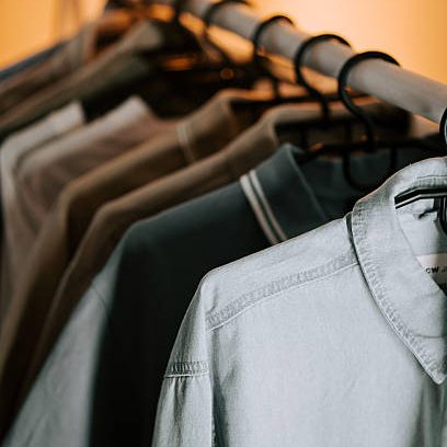 A variety of stylish shirts hang neatly on a rack with warm light illuminating them, showcasing different colors and designs.